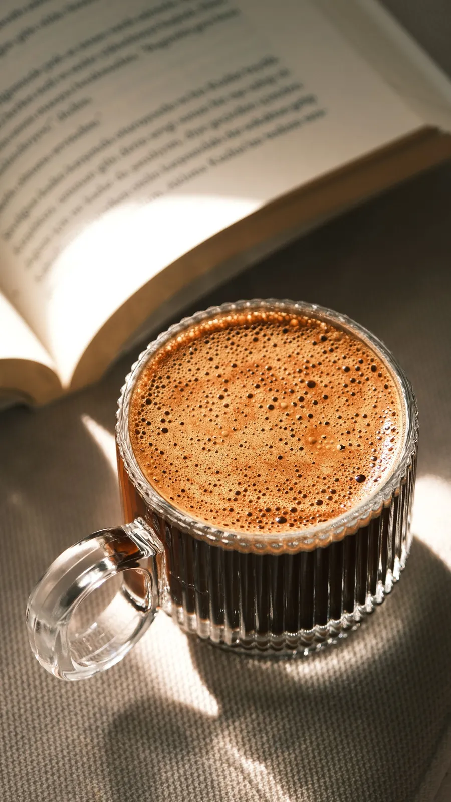 Warm coffee in a glass mug beside an open book