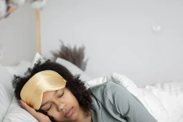 Woman asleep on white pillows wearing a gold sleep mask