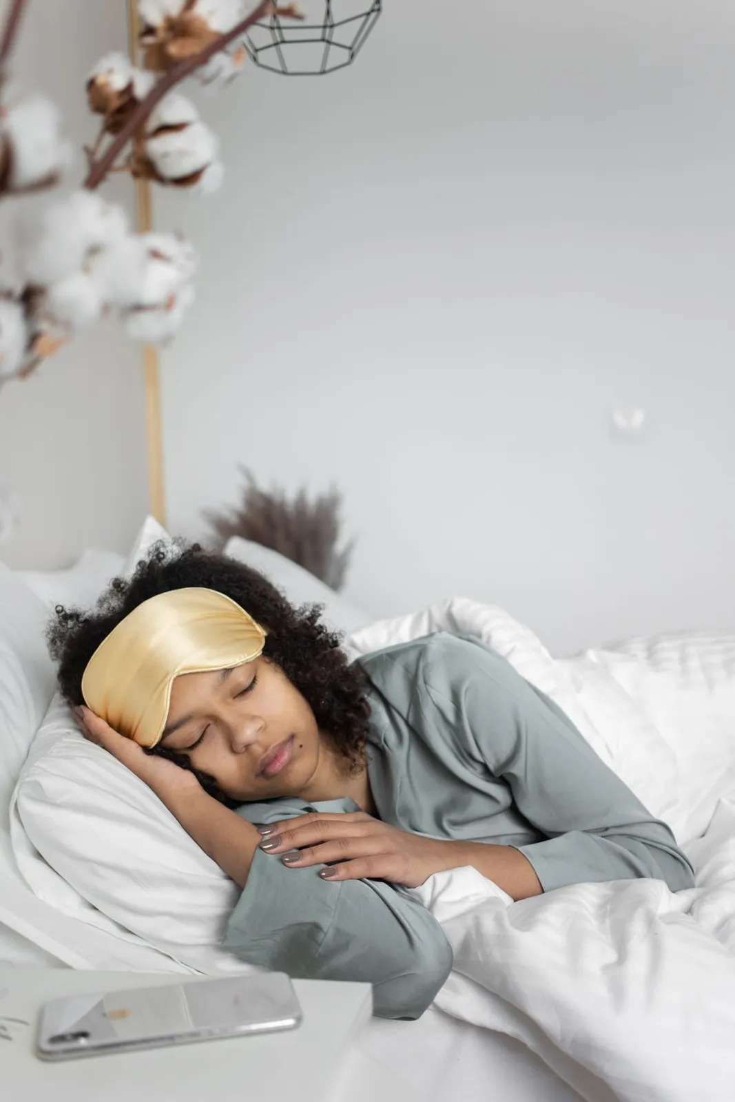 Woman asleep on white pillows wearing a gold sleep mask