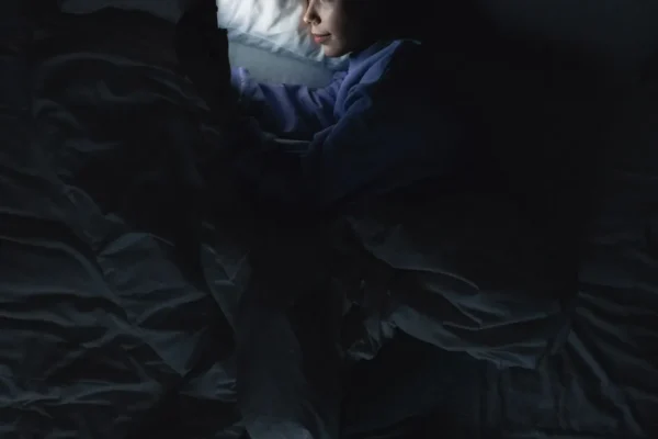 Person lying in a dark bedroom lit only by a phone screen
