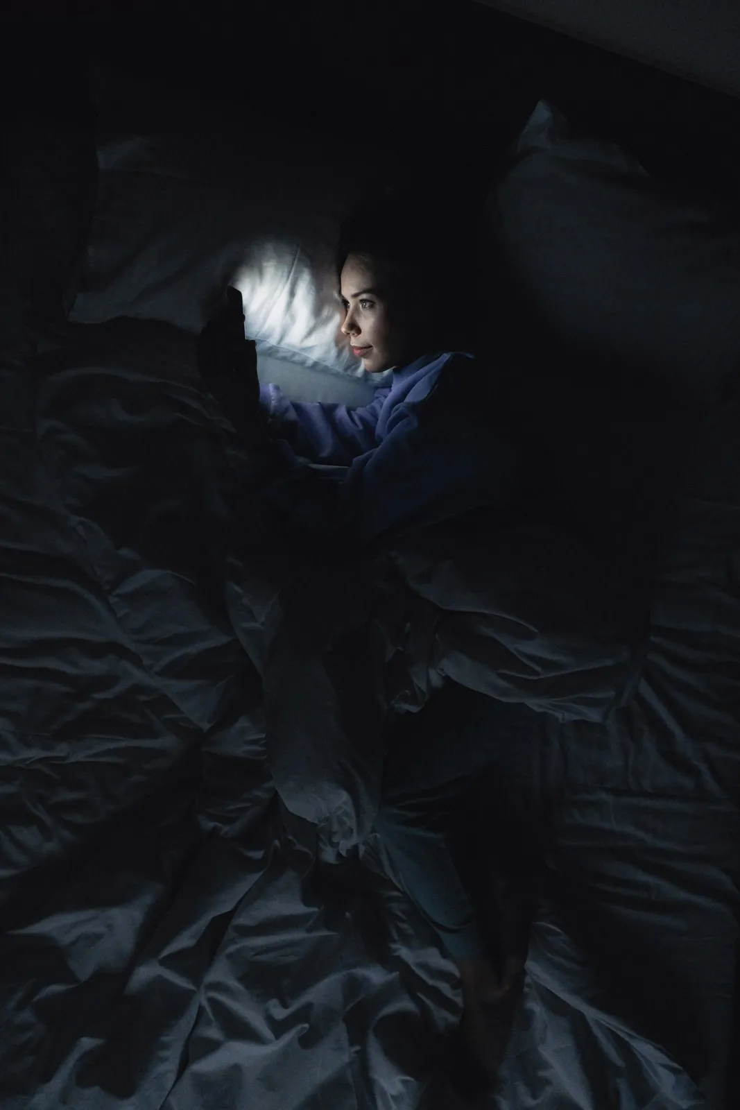 Person lying in a dark bedroom lit only by a phone screen