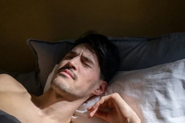 Man resting in bed with eyes closed as early light comes through the window