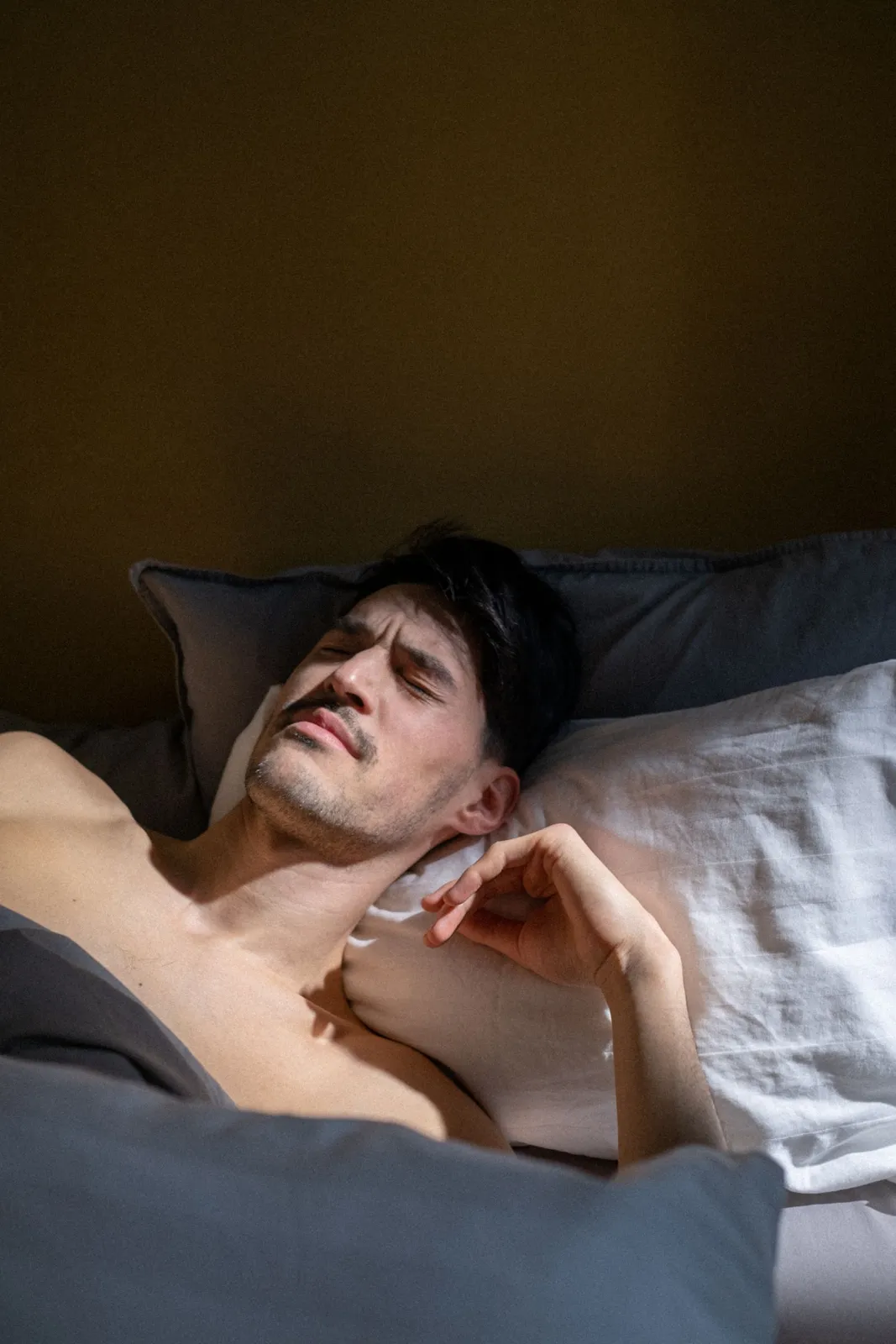 Man resting in bed with eyes closed as early light comes through the window