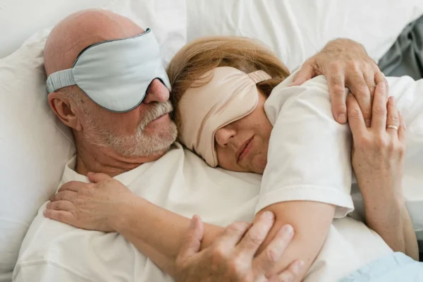 Older couple asleep together in bed wearing sleep masks