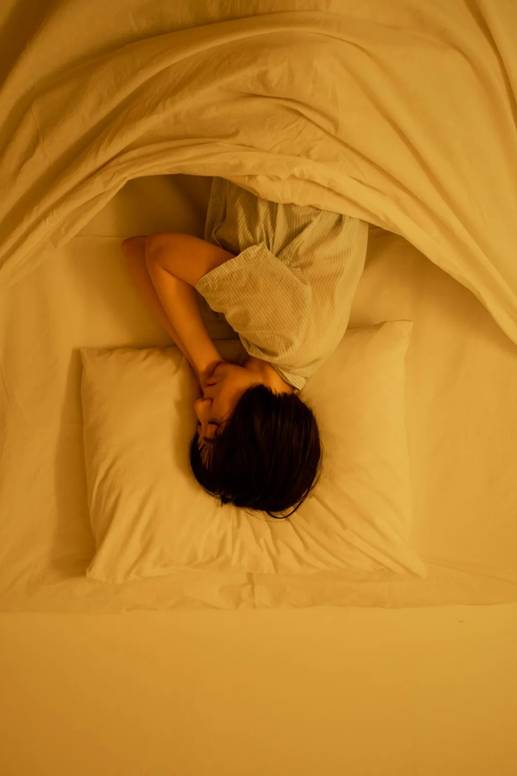 Person curled up asleep under warm yellow bedding