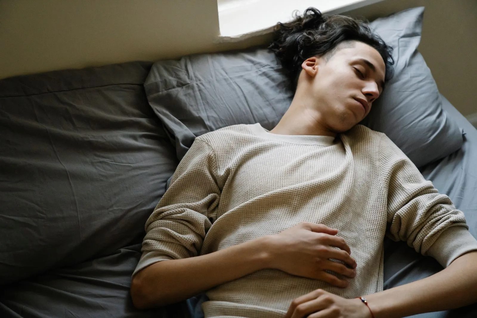 Young man fast asleep on grey bedding